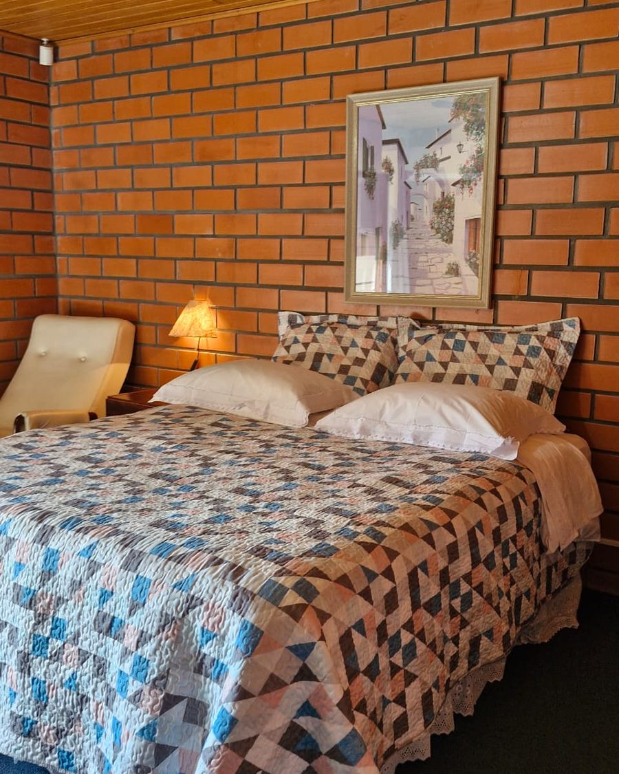 Suíte Casinha - cama, poltrona e parede de tijolo